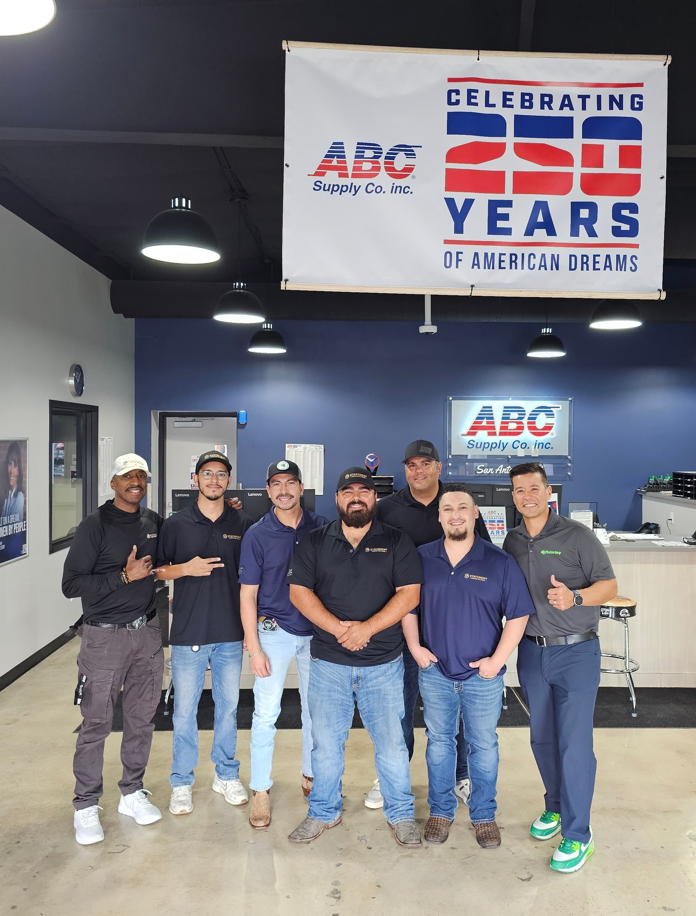 Seven men pose together under a banner celebrating 250 years of ABC Supply Co.